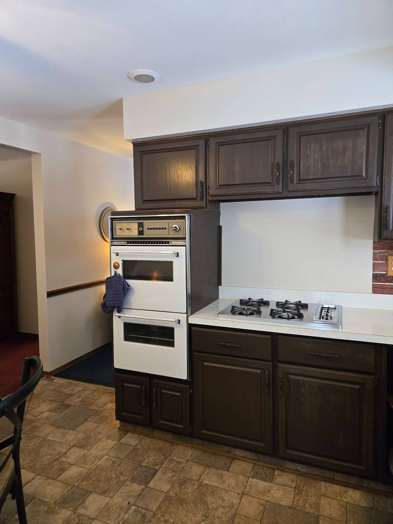 Small kitchen with dark wood cabinets, white countertop, built-in oven, and gas cooktop.