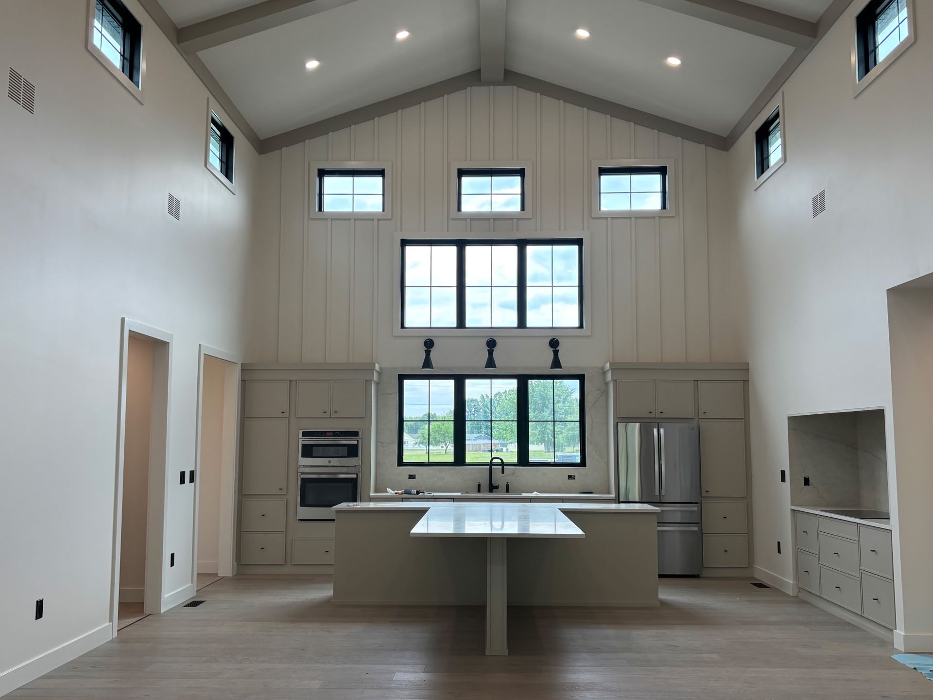 Bright, empty modern kitchen with white cabinets, central island, and large windows and high vaulted ceiling
