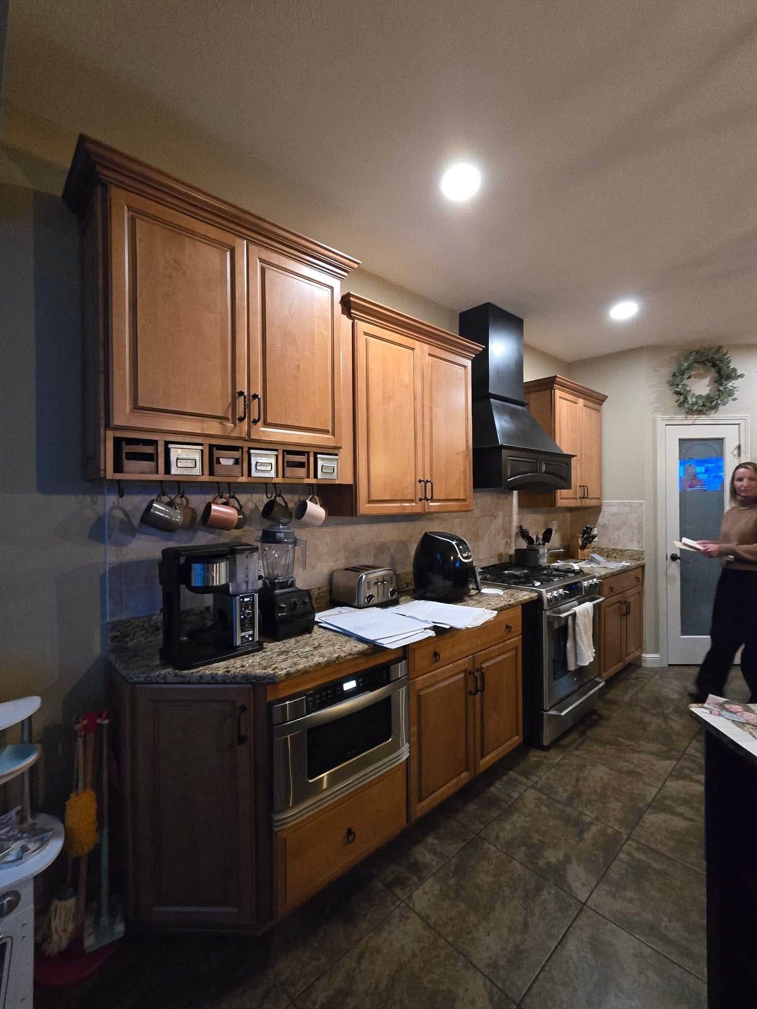 Kitchen with wooden cabinets, dark tile floor, and a person standing near the doorway.