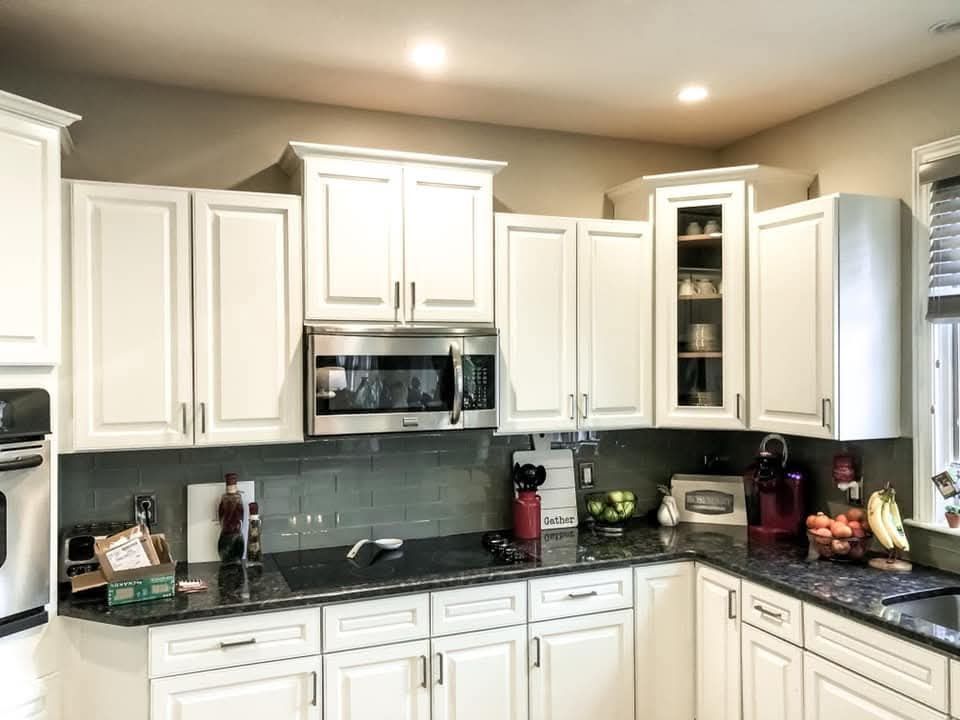 Bright kitchen with white cabinets, black countertops, stainless microwave, and a tiled backsplash.