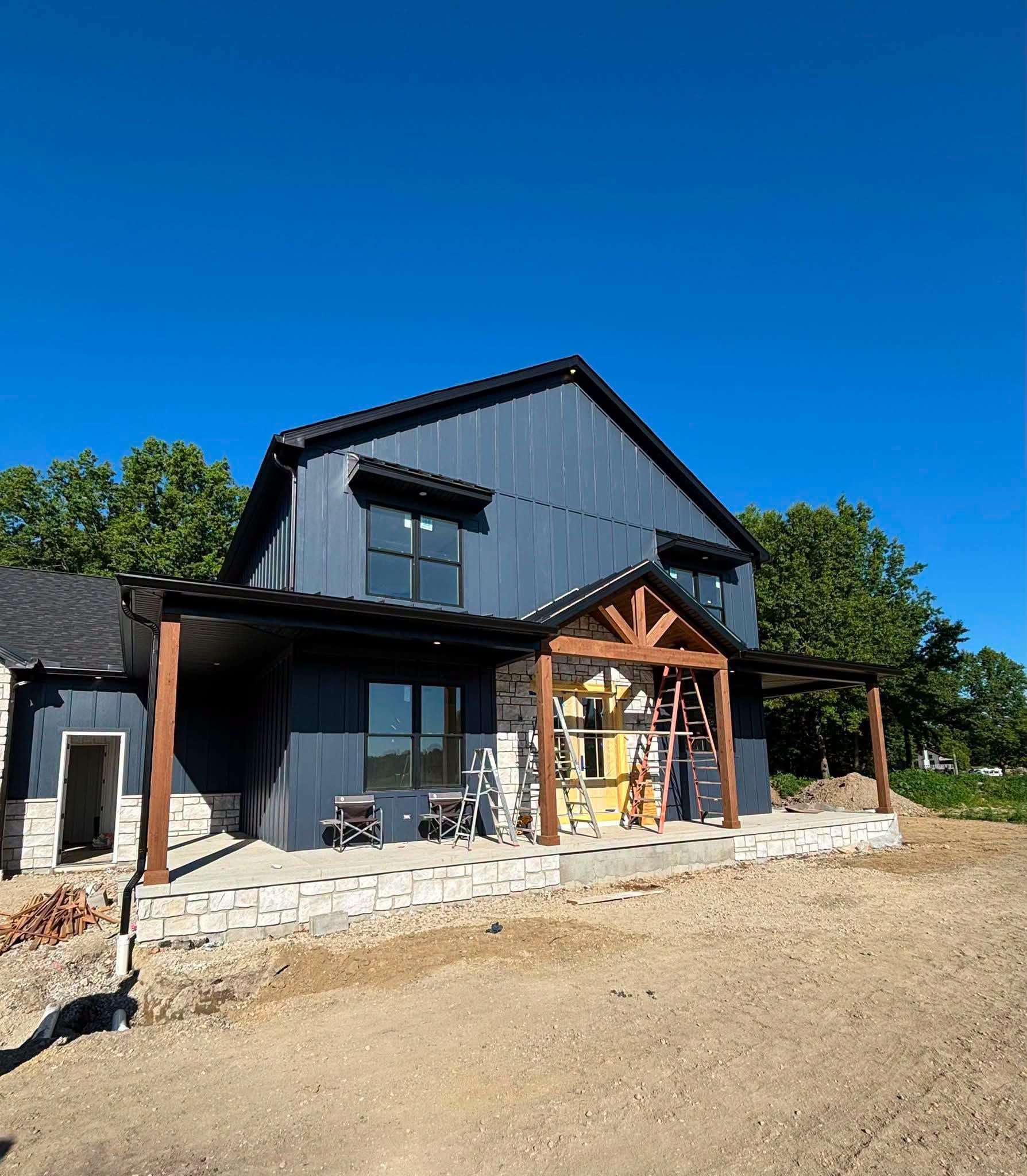 Black barn-style building with wood-framed entrance and stone base under a clear blue sky