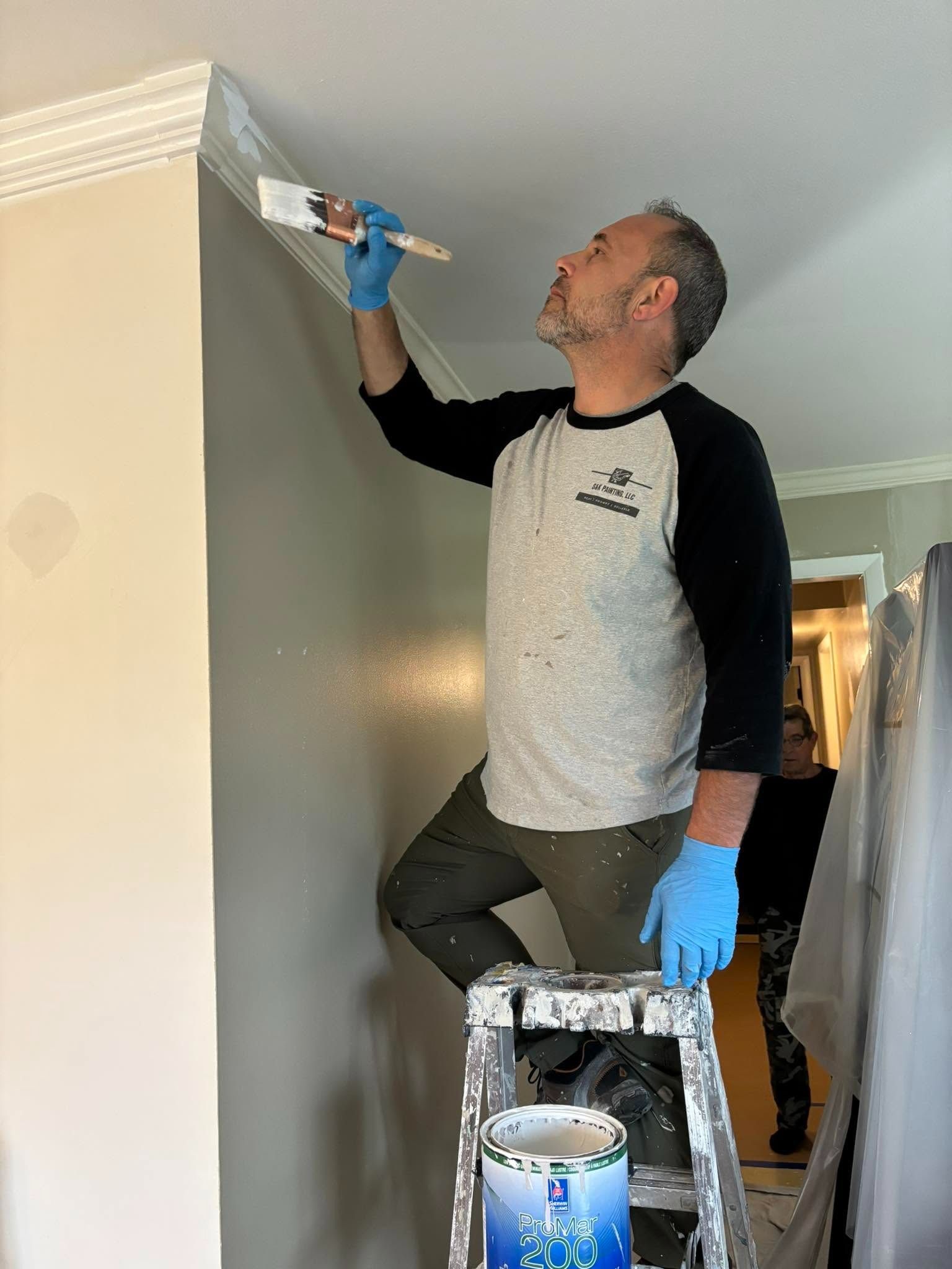 Person on ladder painting a gray wall near the ceiling with a paintbrush and tray