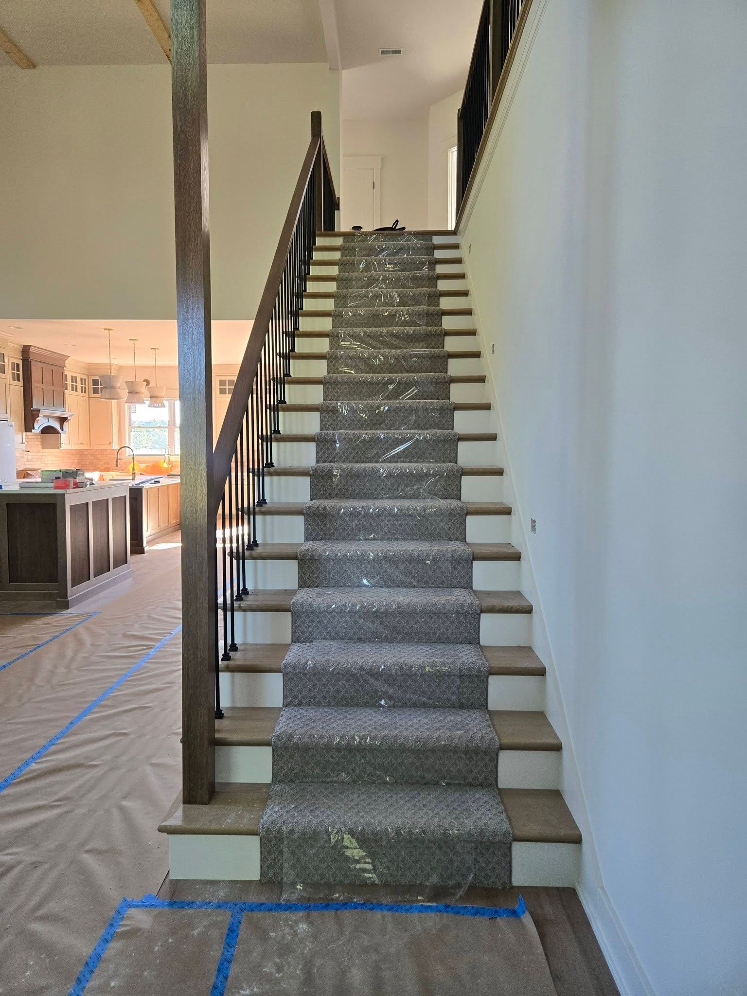 Carpeted staircase under construction, with blue painter’s tape at the bottom and kitchen area visible left