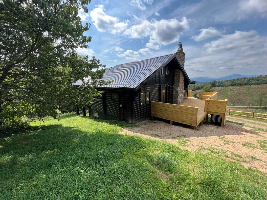 a small cabin with a deck is sitting on top of a grassy hill .