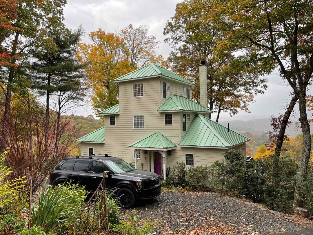 a house with a green roof and a black suv parked in front of it .