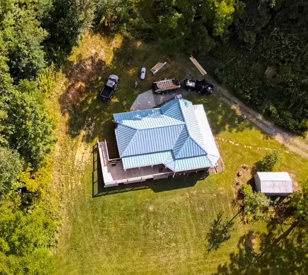 an aerial view of a house with a blue roof surrounded by trees .