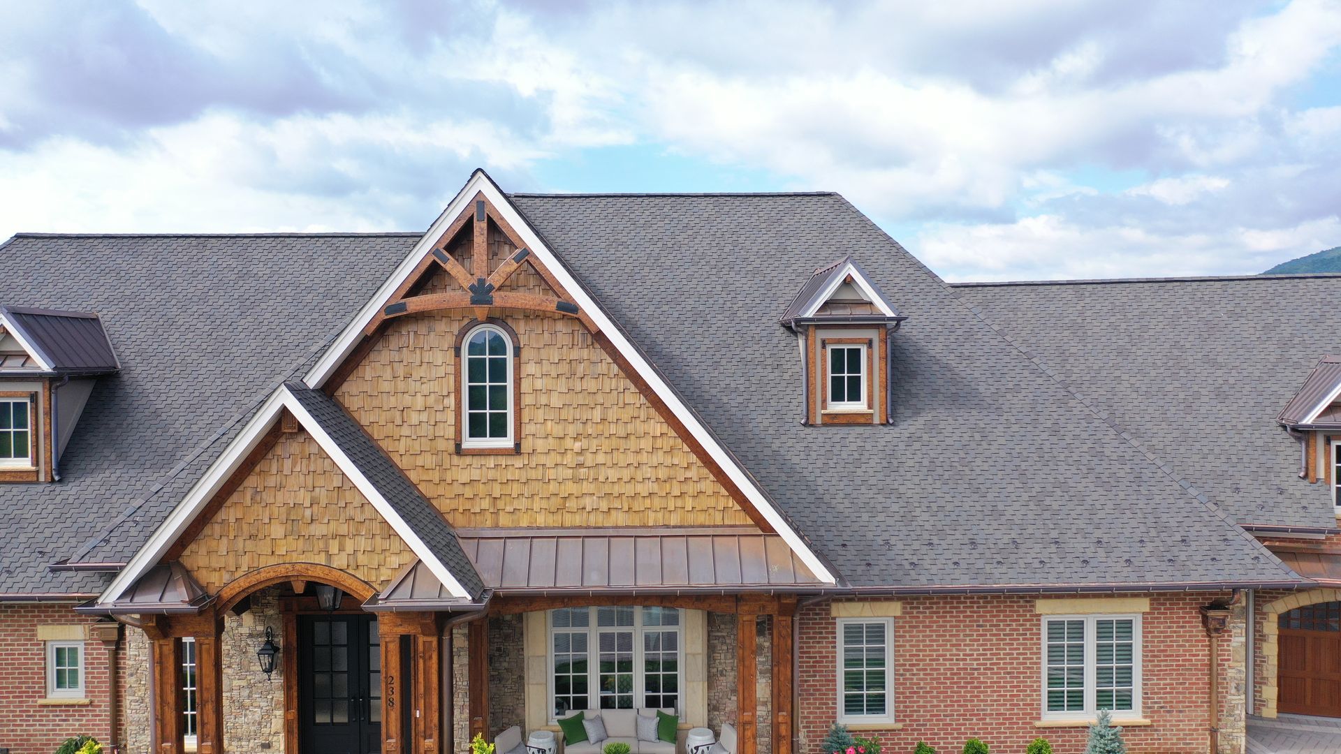 Brick house with cedar shake roof and wood accents, cloudy sky.