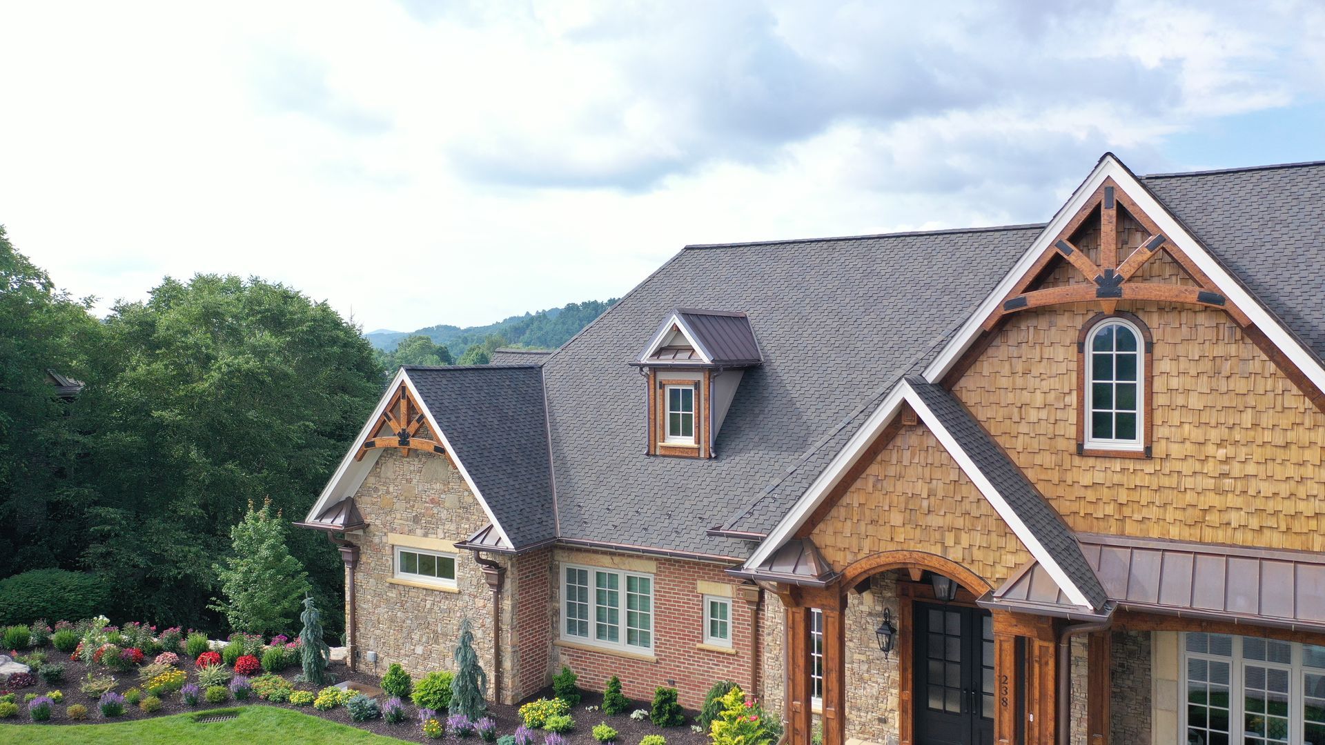 Stone and wood-trimmed house with a dark roof, overlooking a green landscape under a cloudy sky.