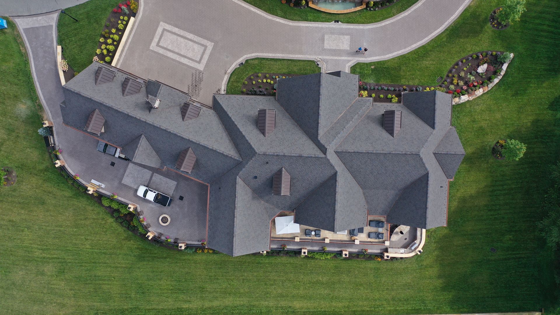Overhead view of a large house with a dark roof, driveway, and surrounding green lawn.