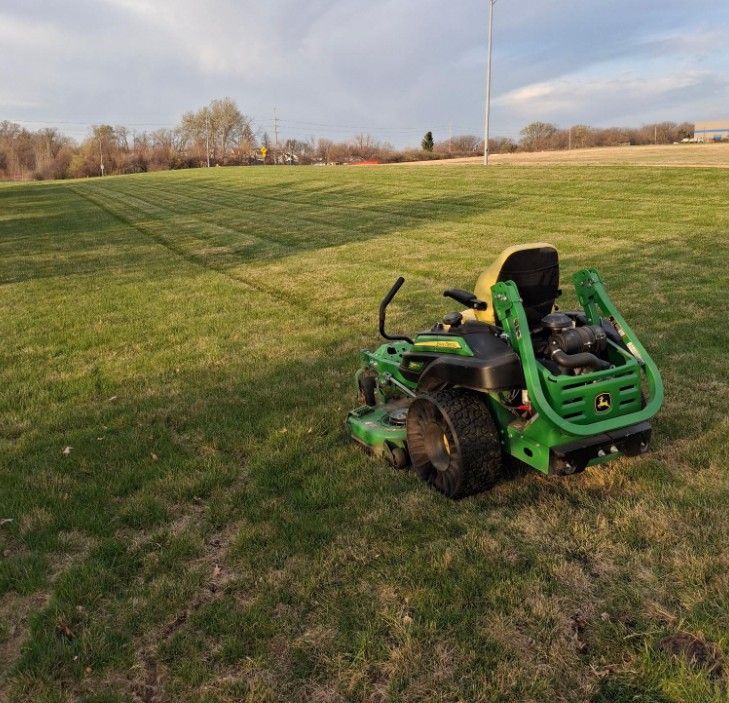 Green riding lawn mower on a grassy field at sunset