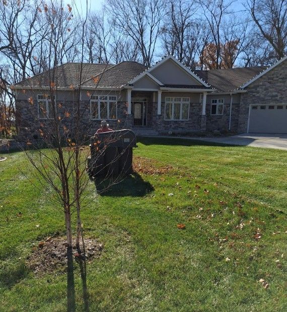 Stone house with a two-car garage and front lawn, viewed from the driveway on a sunny day