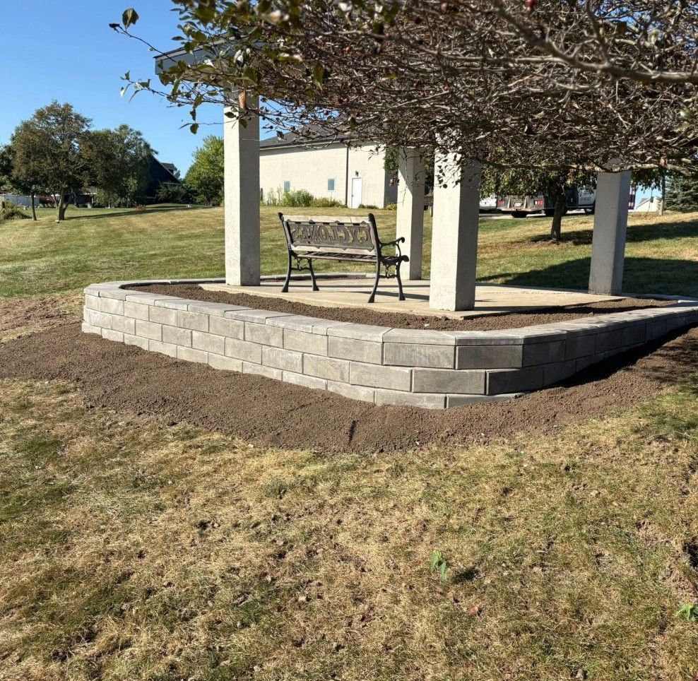 Bench under a vine-covered pergola on a raised stone patio in a grassy park