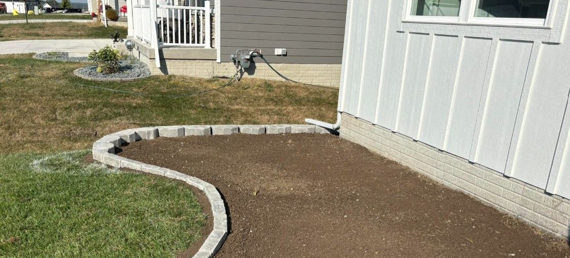 Freshly landscaped yard with curved concrete border and brown mulch beside a white house