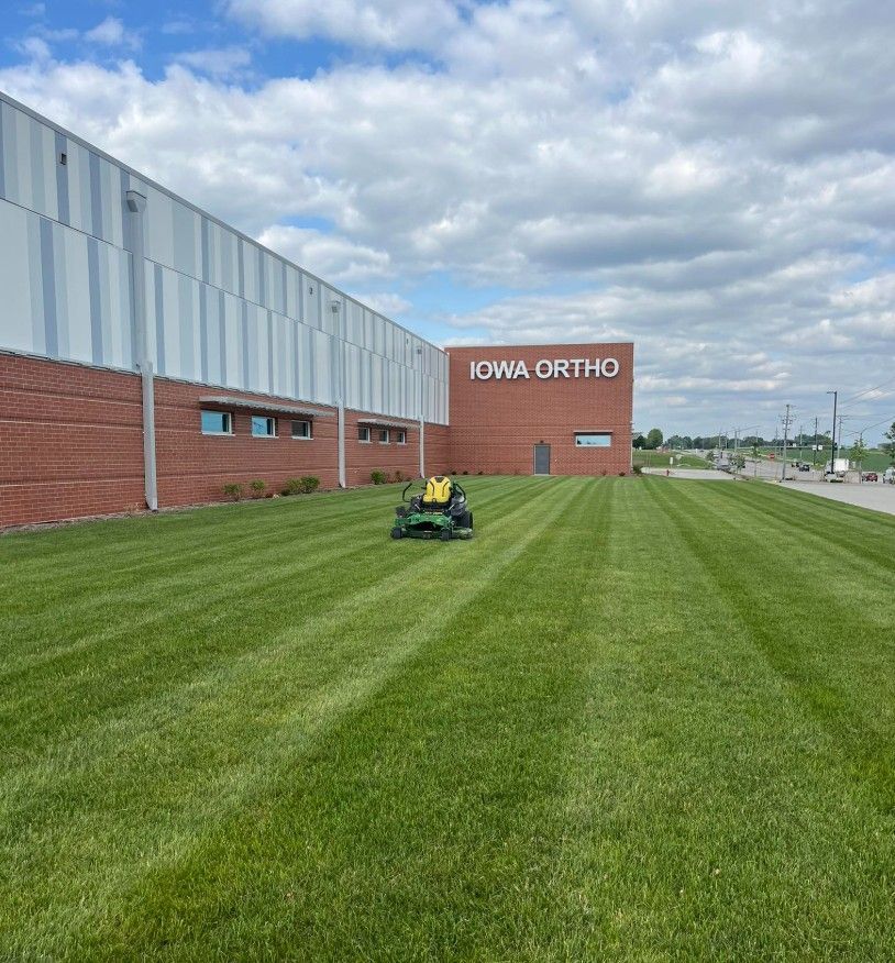 Mowed lawn beside Iowa Ortho building, with a person on a lawn tractor under a cloudy sky