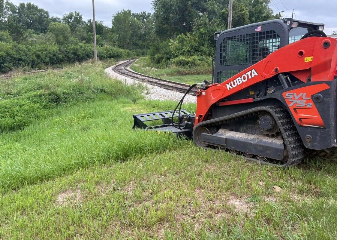 Orange Kubota skid steer beside a curving dirt path in a green field under cloudy skies