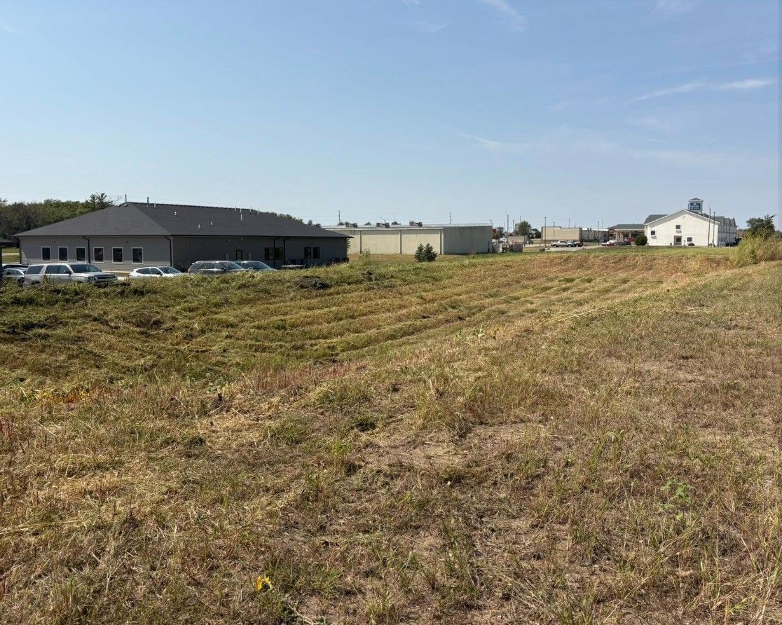 Grassy field with low industrial buildings under a clear blue sky