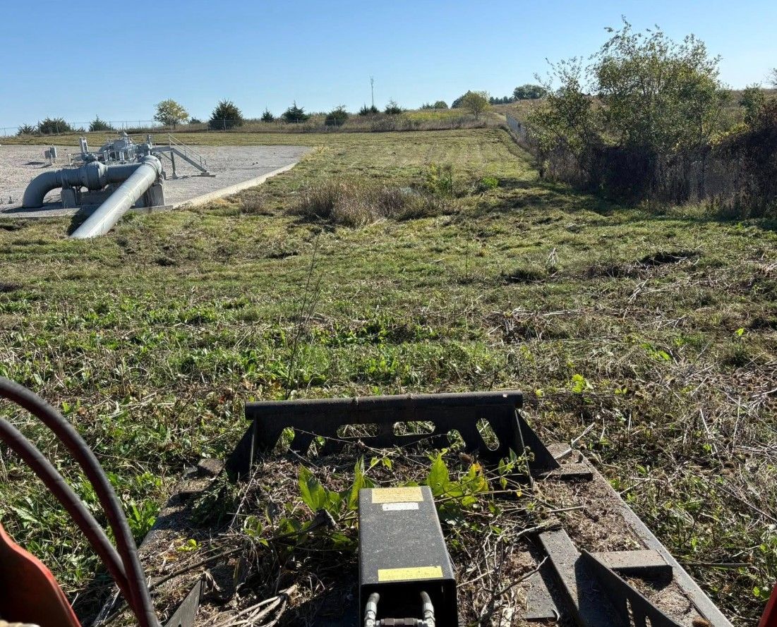 Farm field with a culvert pipe, dirt mound, and brush under a clear sky