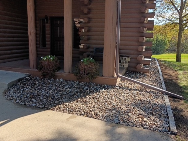 Log cabin corner with gravel landscaping and a concrete walkway beside a grassy yard.
