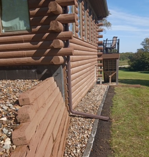 Log cabin exterior with log siding, rock landscaping, and a small balcony beside a grassy yard