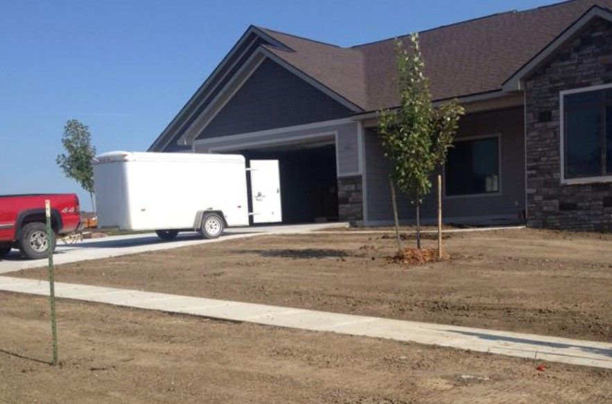 A red pickup truck is parked in a driveway, towing a white enclosed trailer into the garage of a suburban home.