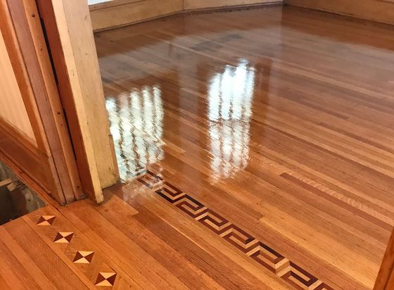 Shiny hardwood floor with decorative border, reflection of the window.