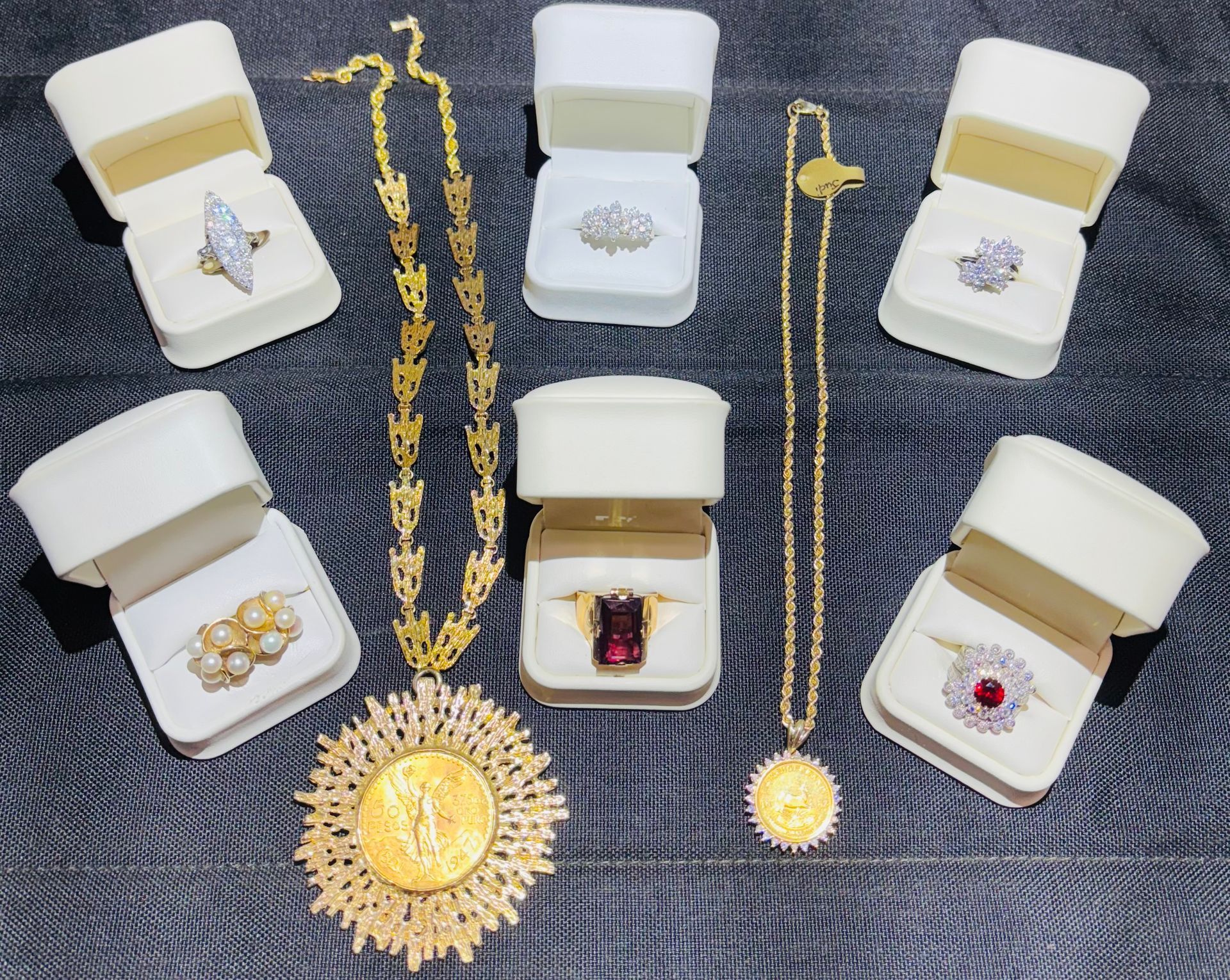 Jewelry display: Gold necklaces, rings in boxes with diamonds, rubies, and pearls, on a dark surface.