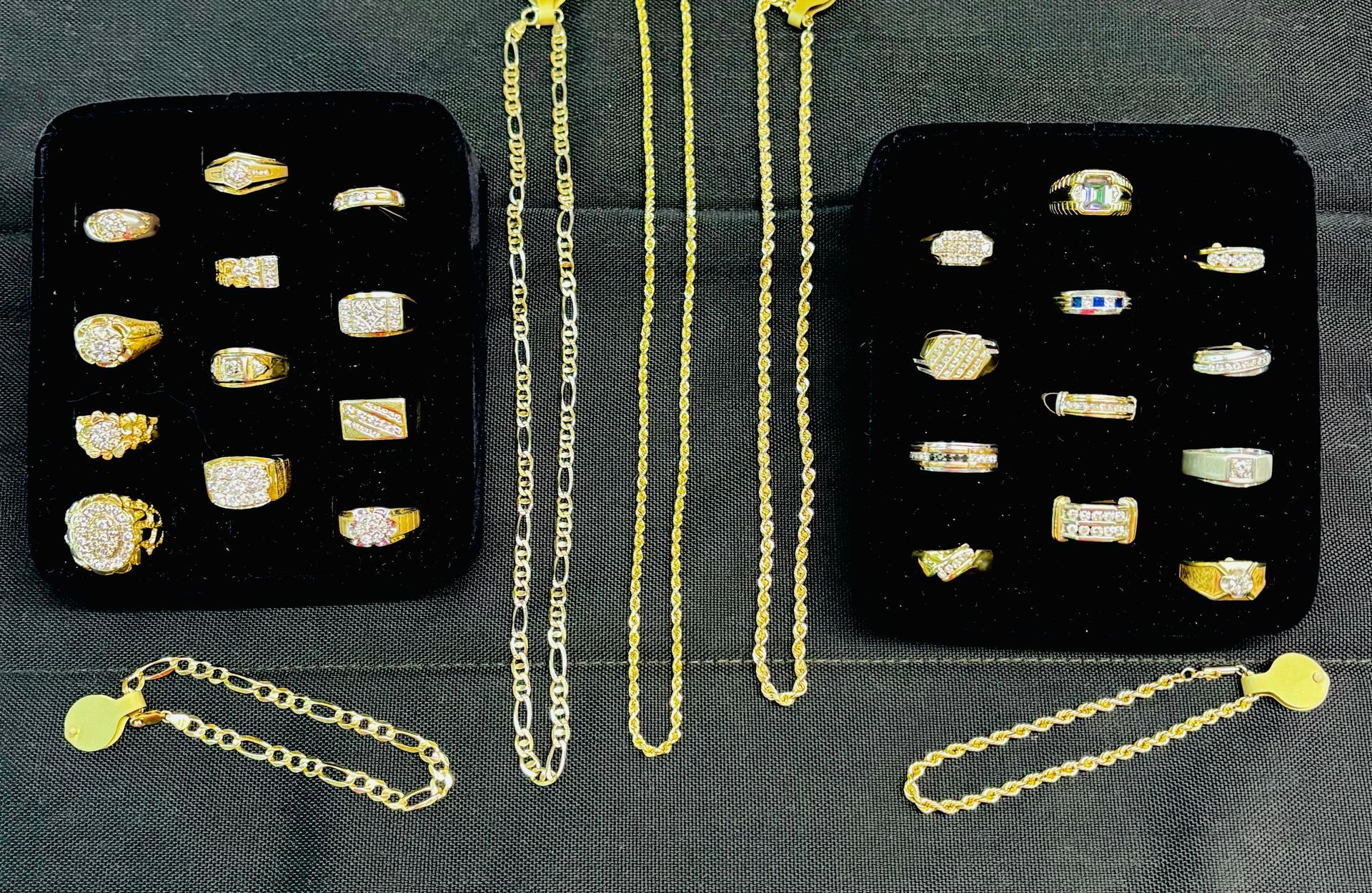 Jewelry display: gold rings and chains arranged on black velvet, reflecting light.