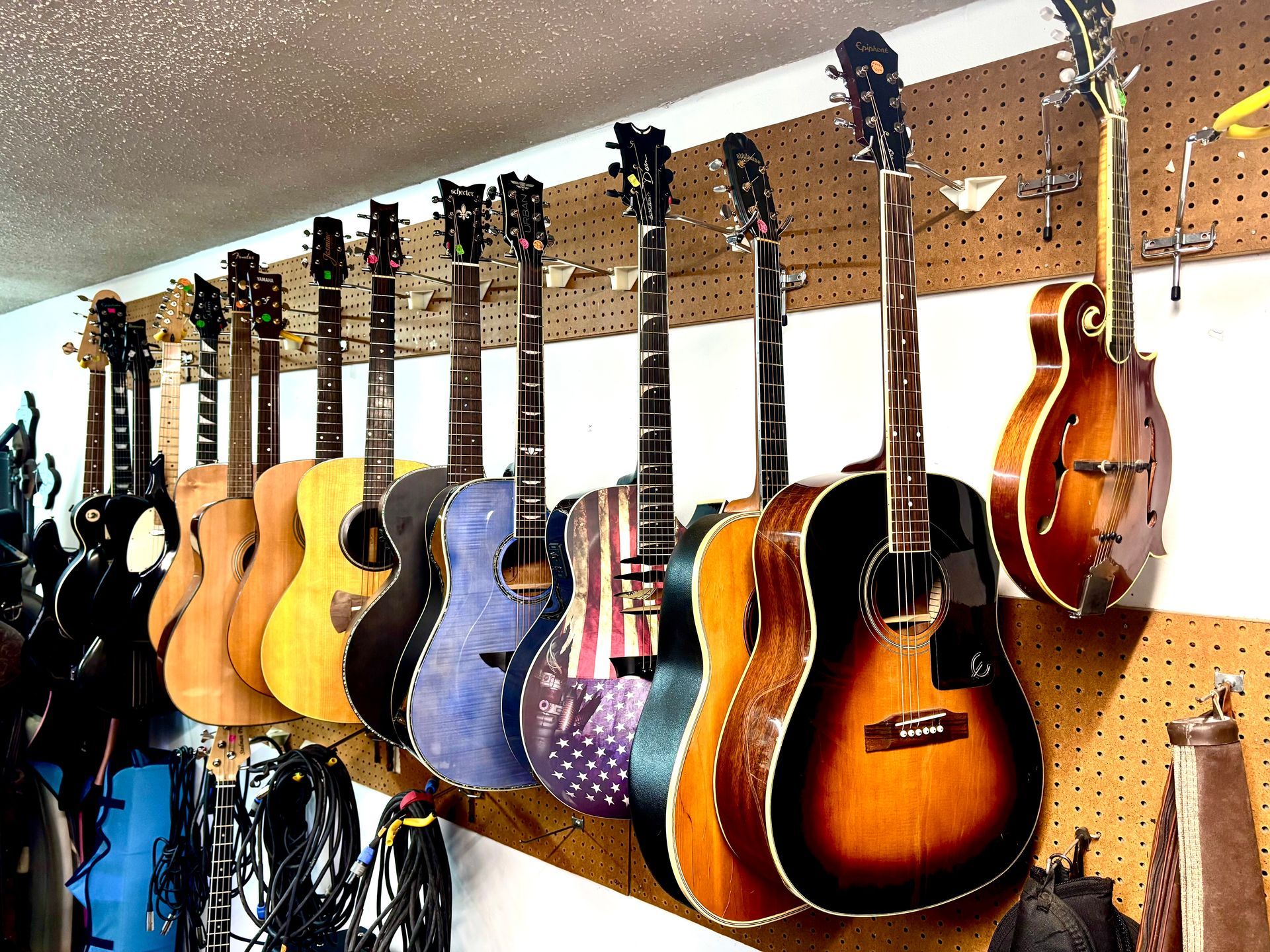 A collection of acoustic guitars hanging on a pegboard wall. Various wood tones and designs are visible.