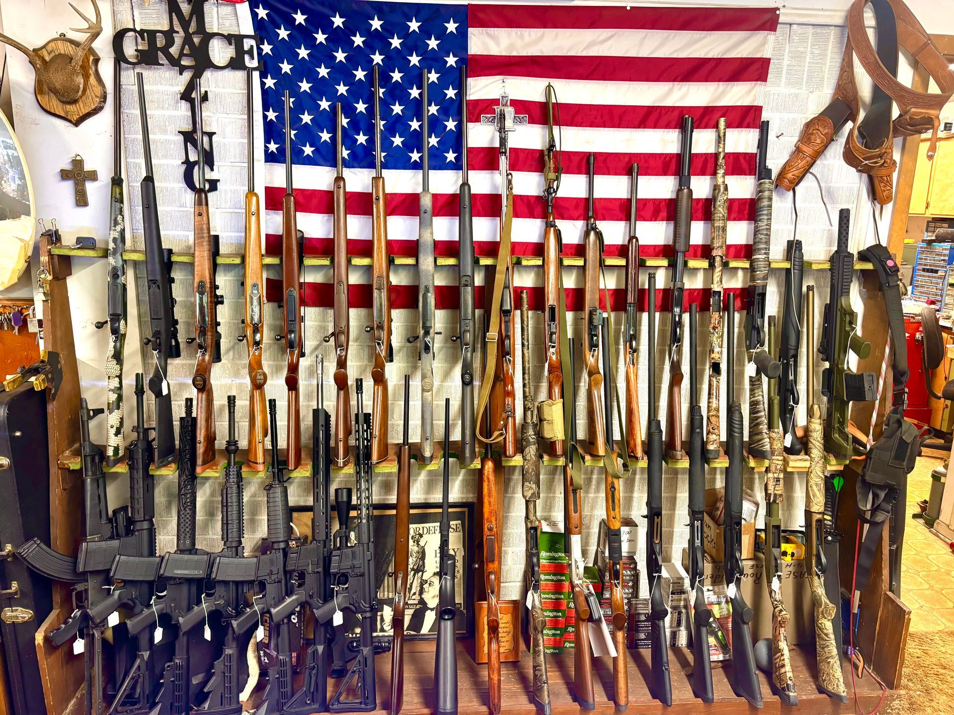 A wall displaying numerous rifles in front of an American flag.