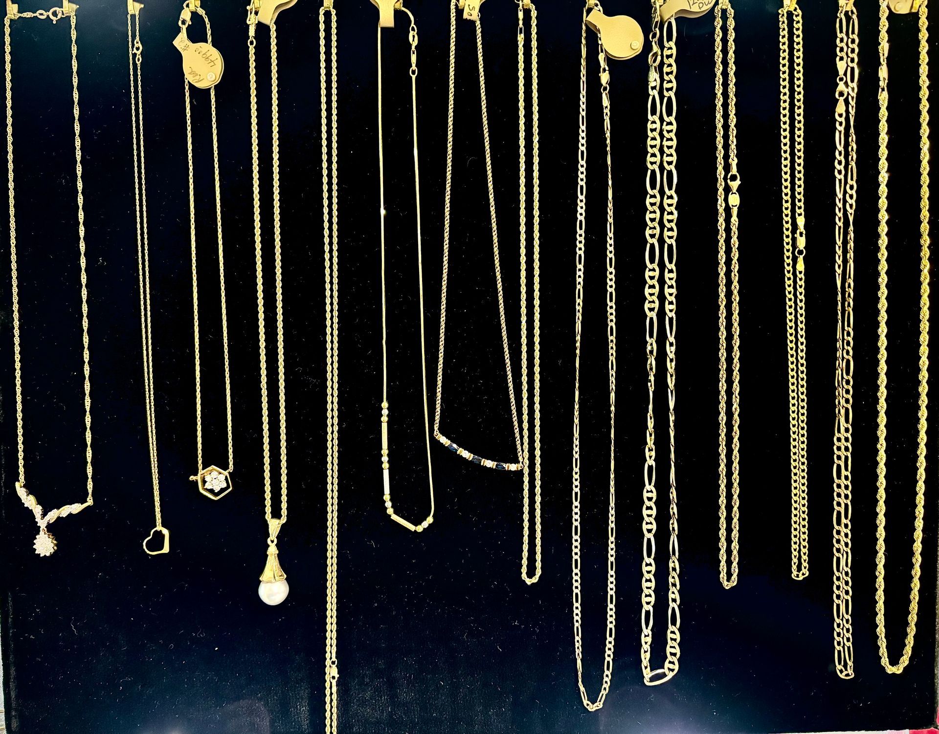 Gold necklaces hanging against a dark background, various styles.