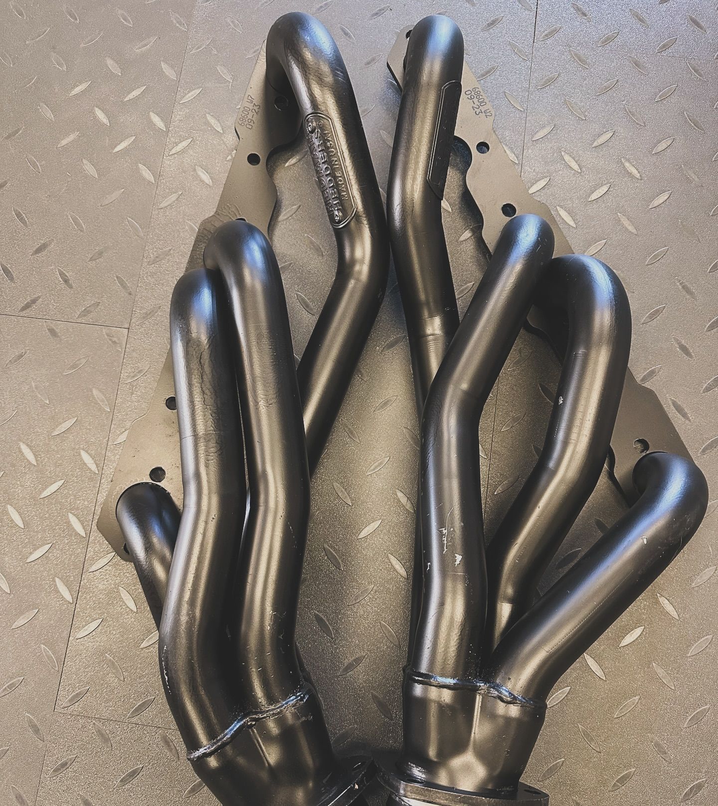 A close up of a black exhaust manifold on a checkered floor