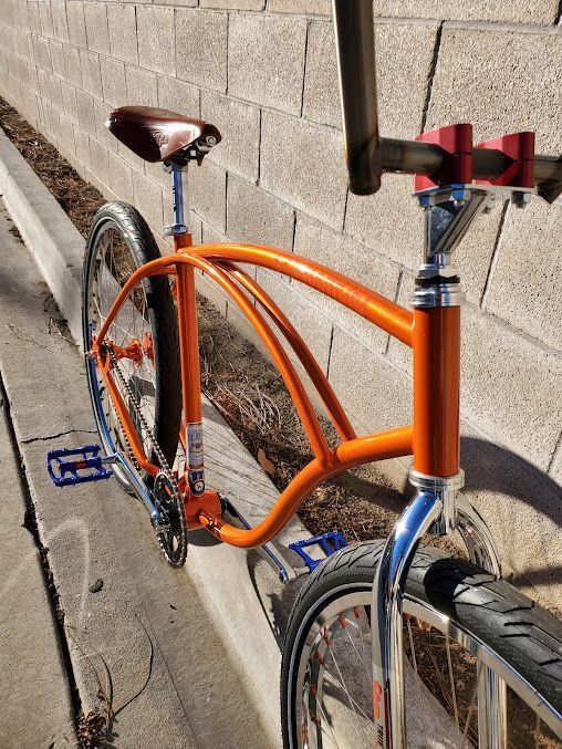 An orange bicycle is parked on a curb next to a brick wall