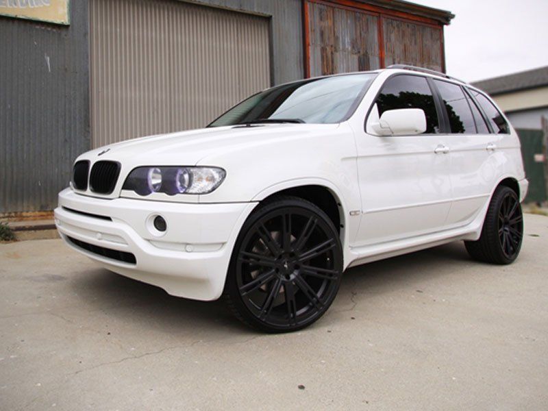 A white bmw x5 with black wheels is parked in front of a building.