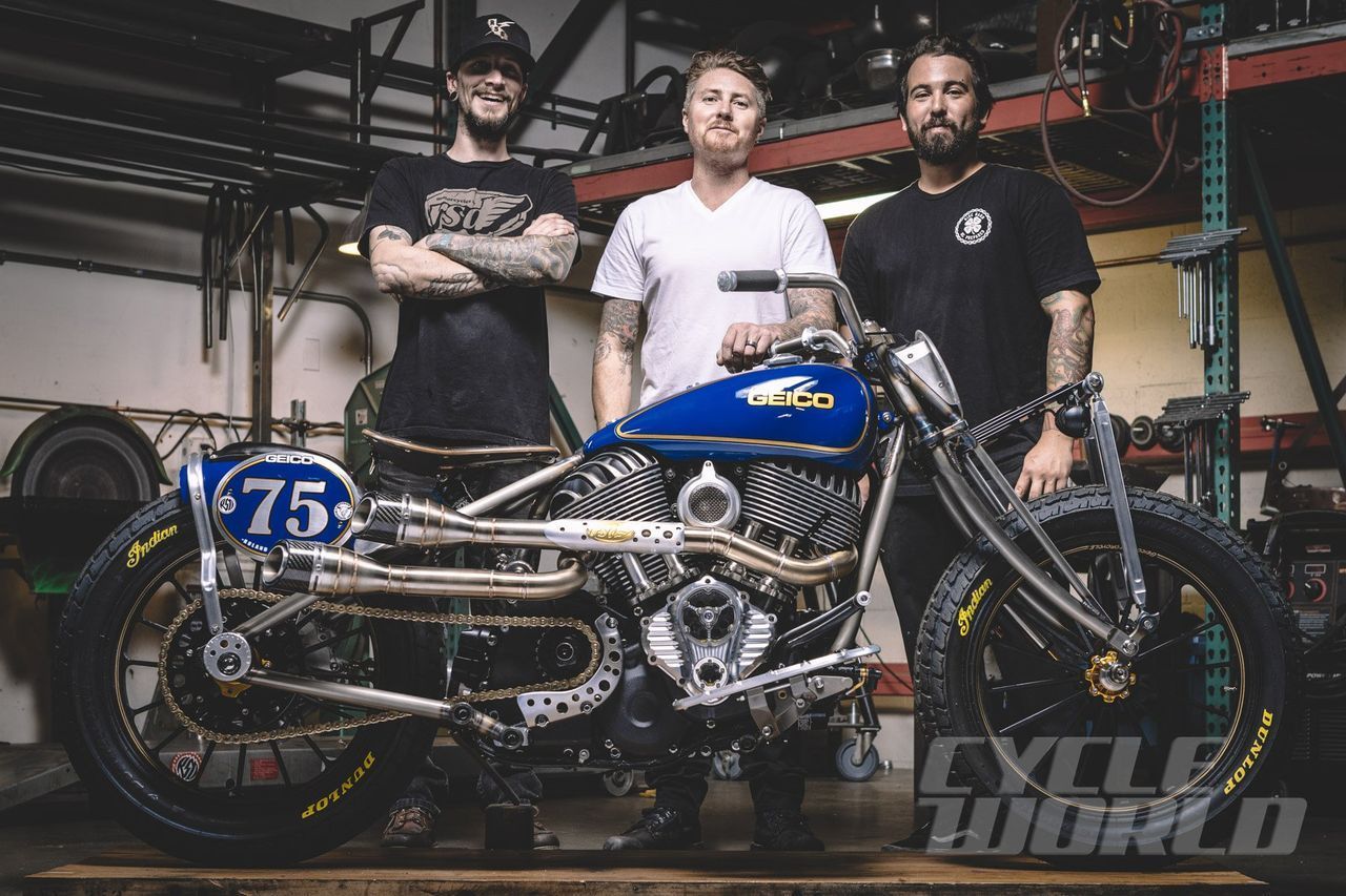 Three men are standing next to a motorcycle with the number 75 on it.