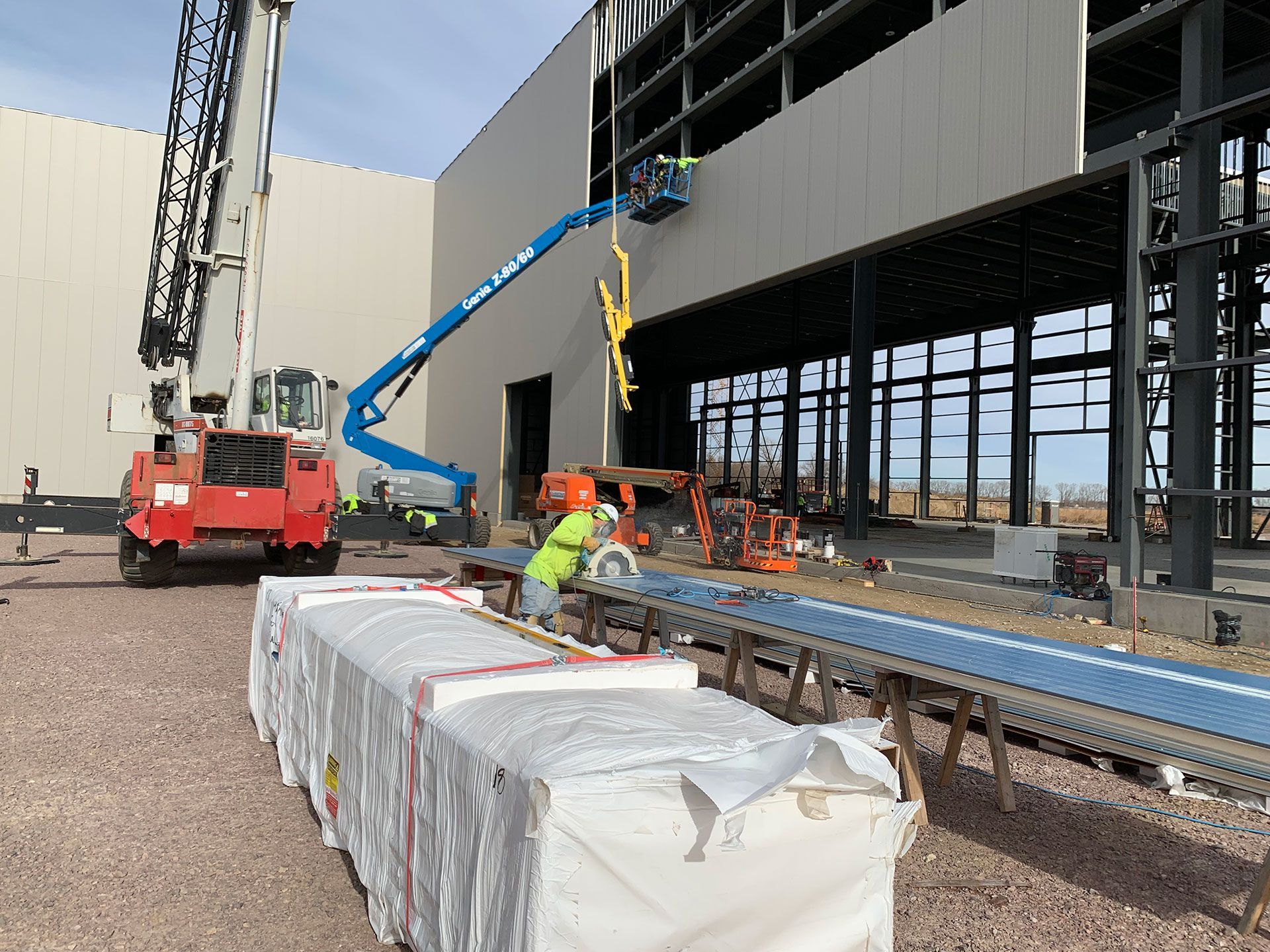 a man cutting a long metal panel in front of a building under construction