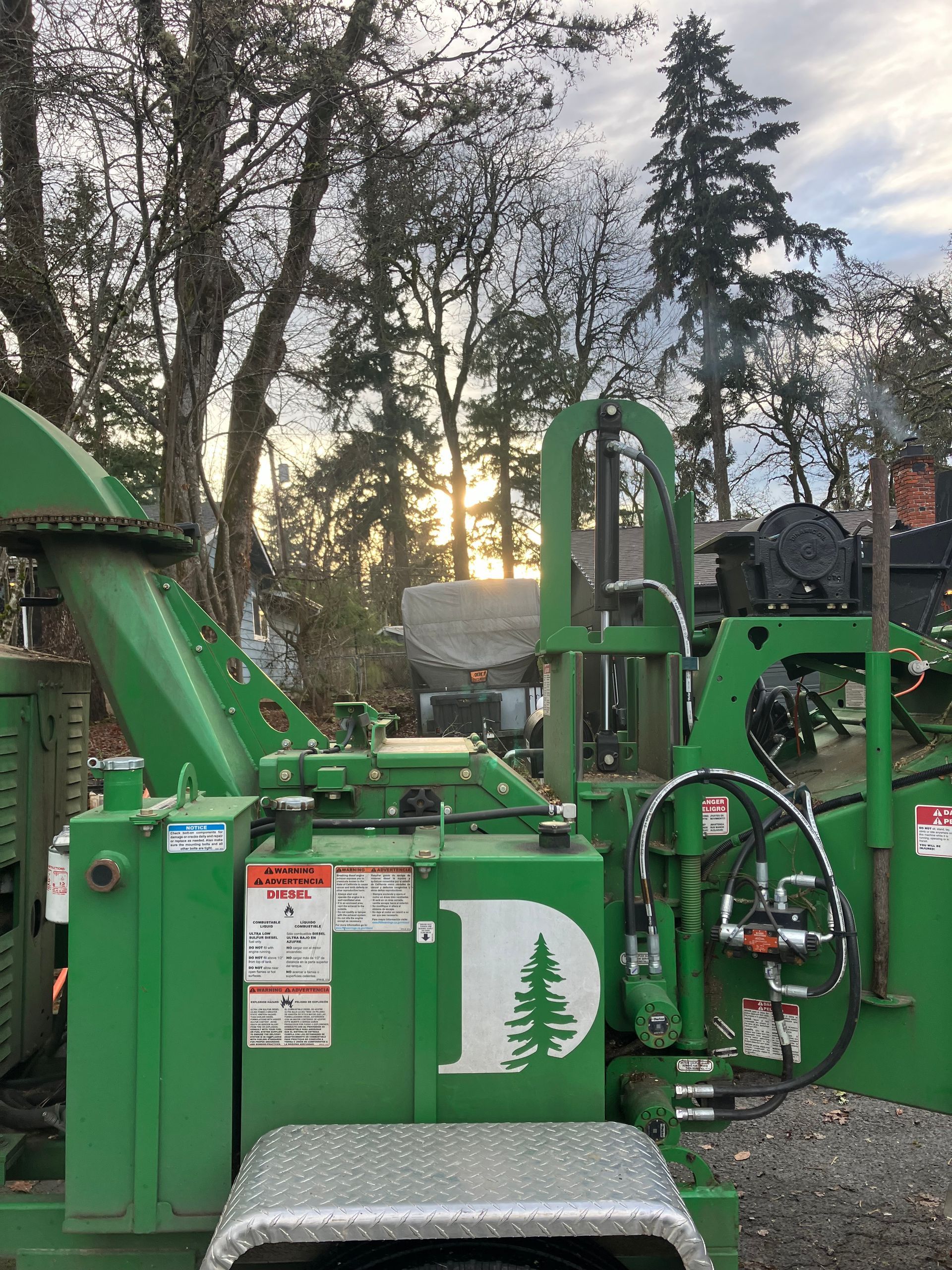 A green tree chipper is parked in front of a forest.