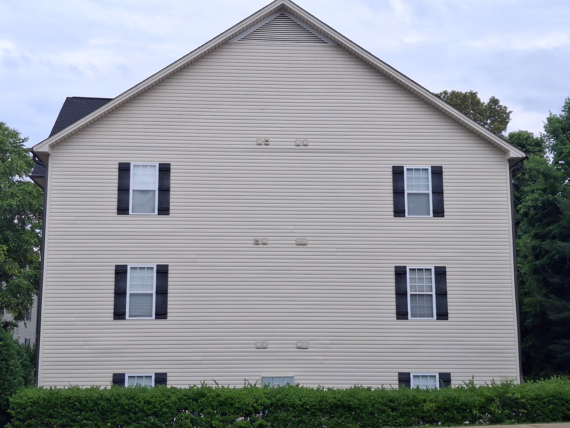 Side view of a beige two-story house with black shutters and a gabled roof.