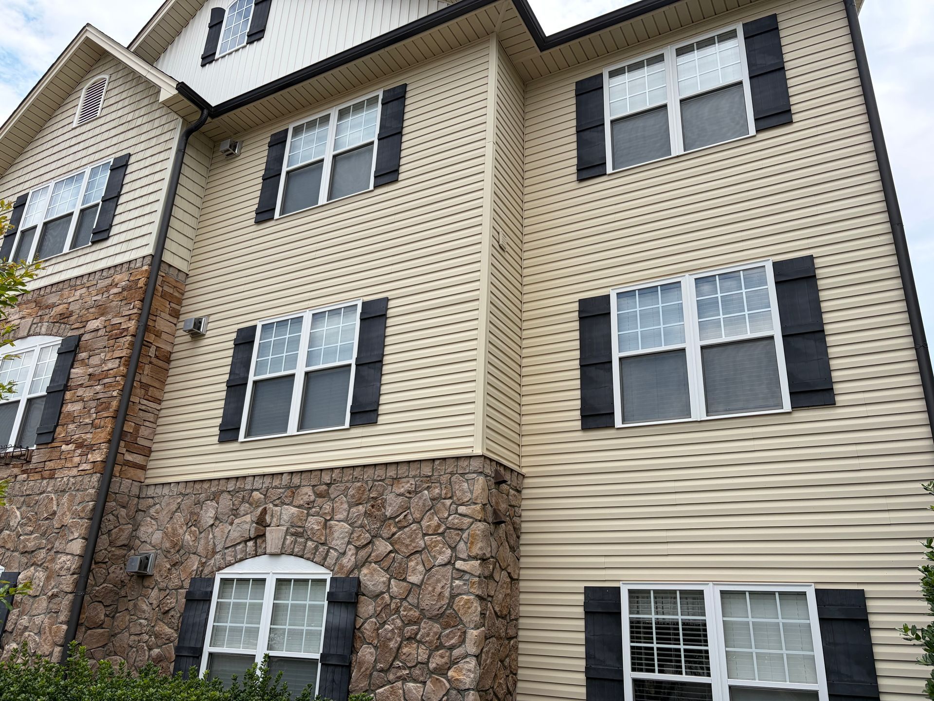 Multi-story apartment building with beige siding, stone accents, and white-trimmed windows