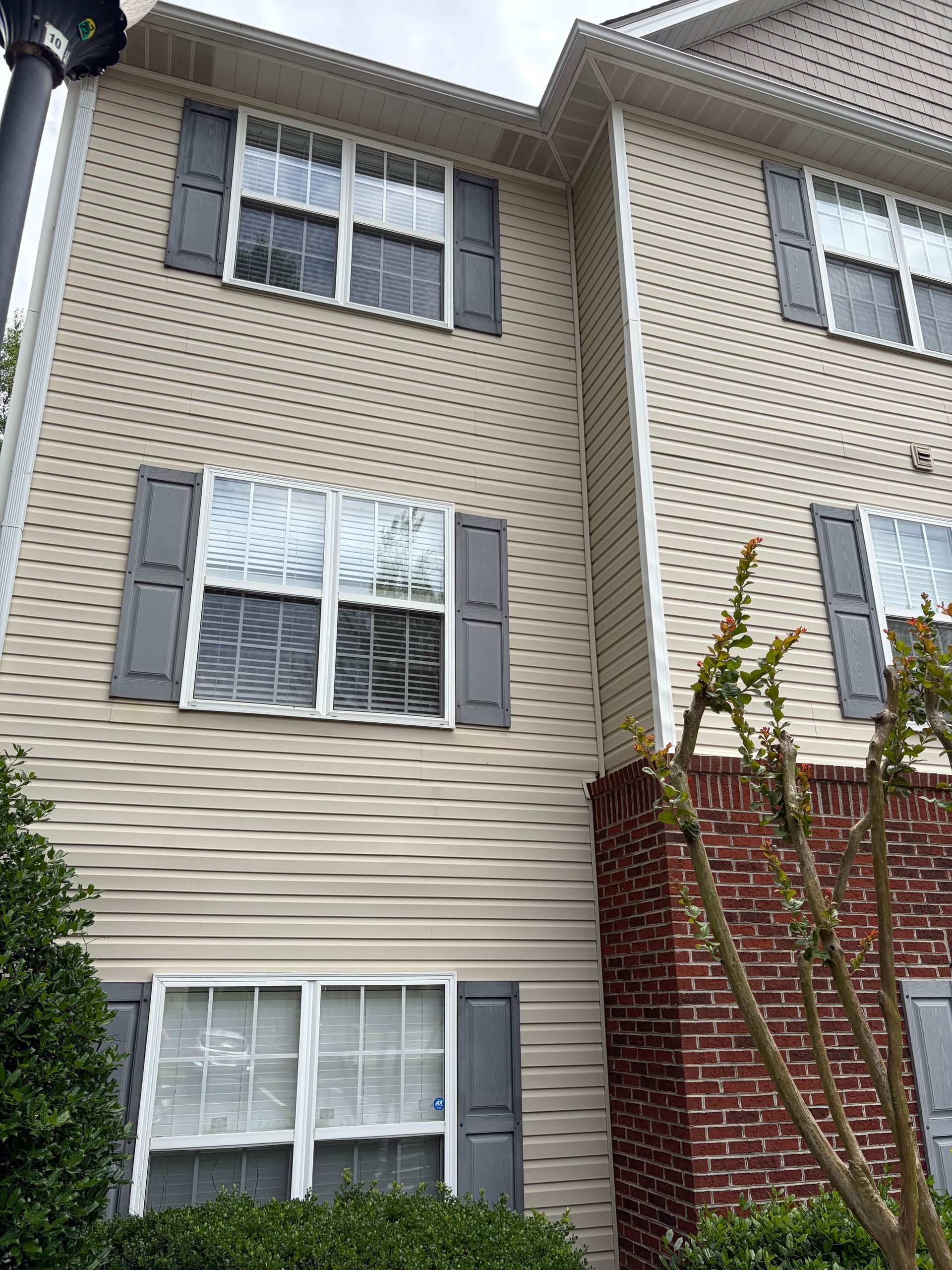 Multi-story beige apartment building with white-trimmed windows and gray shutters under an overcast sky