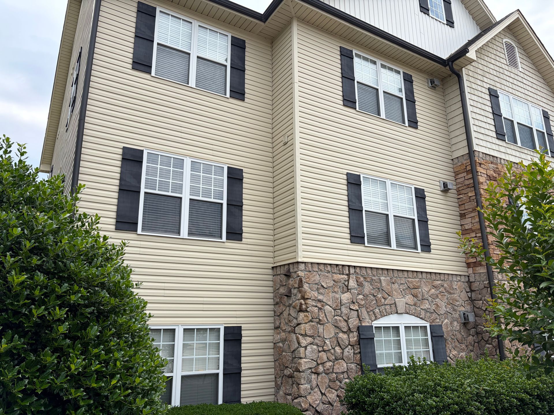 Apartment building exterior with beige siding, stone facade, and multiple windows.