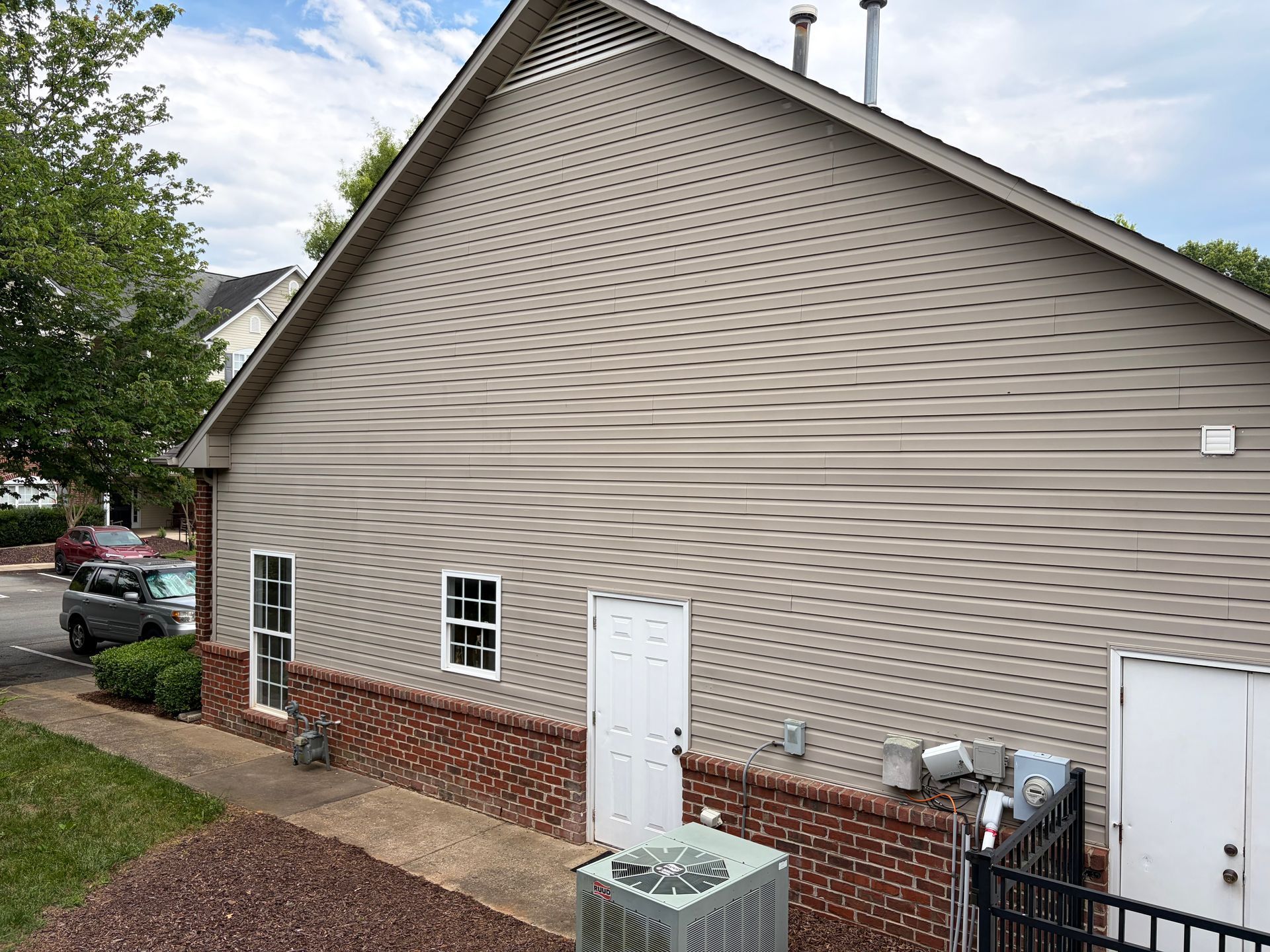 Side of a beige house with brick foundation, white doors, small windows, and outdoor utility equipment.