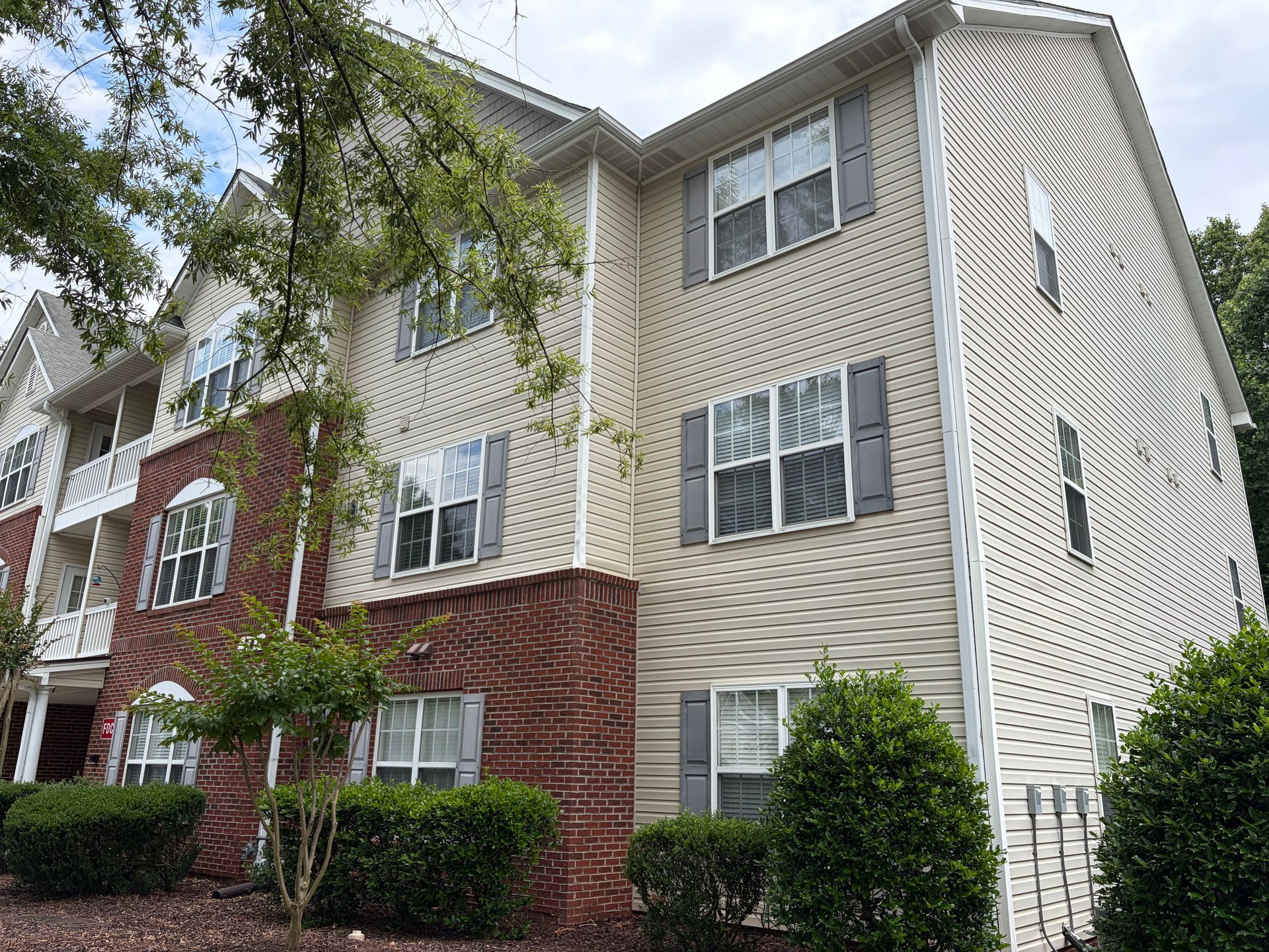 Three-story apartment building with beige, red brick, and white siding, viewed from a landscaped courtyard.