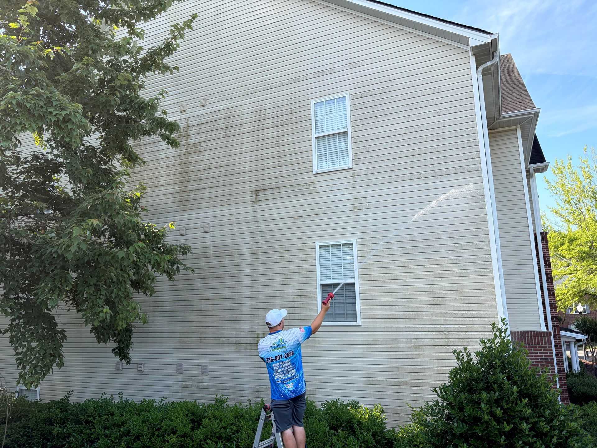 Person in blue shirt and white cap points at an upper-story window on a beige house.