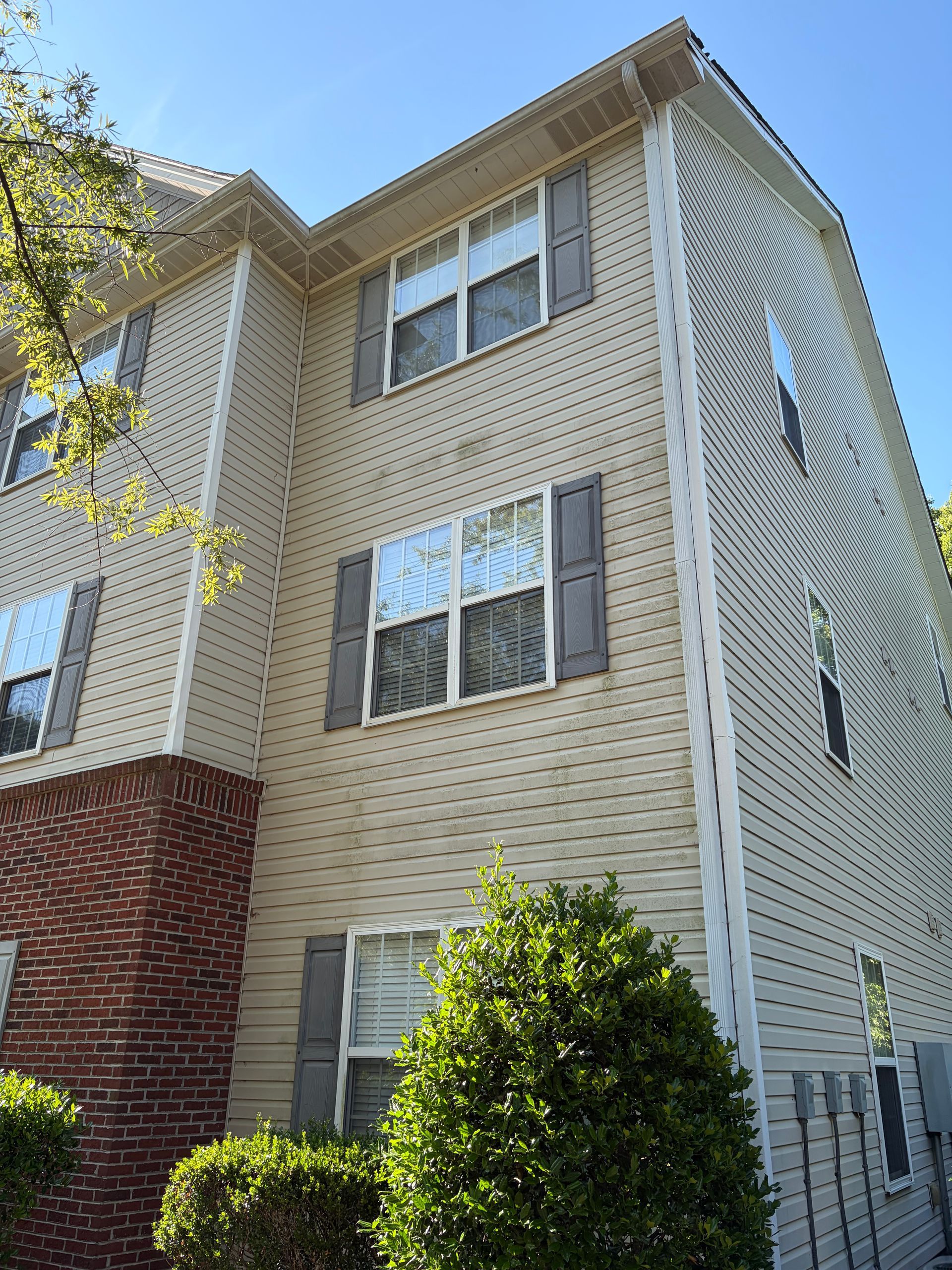 Exterior of a beige brick apartment building with white-trimmed windows and shrubbery in front