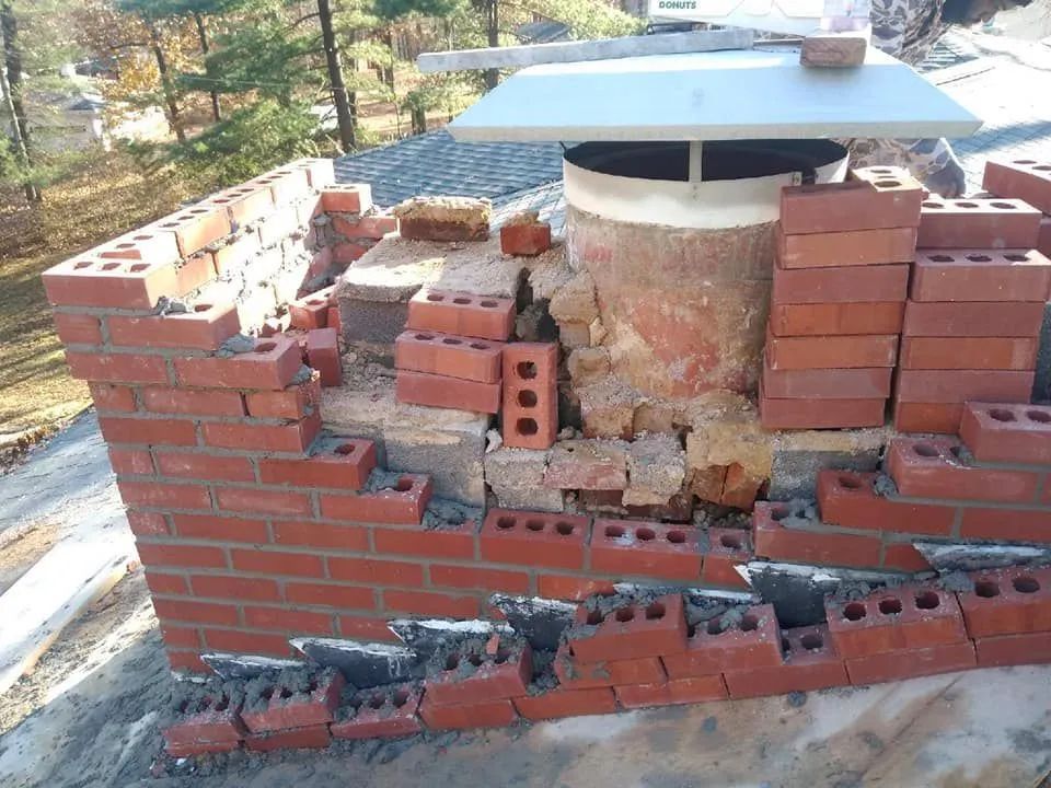 Partially collapsed brick chimney on a rooftop with loose and broken red bricks