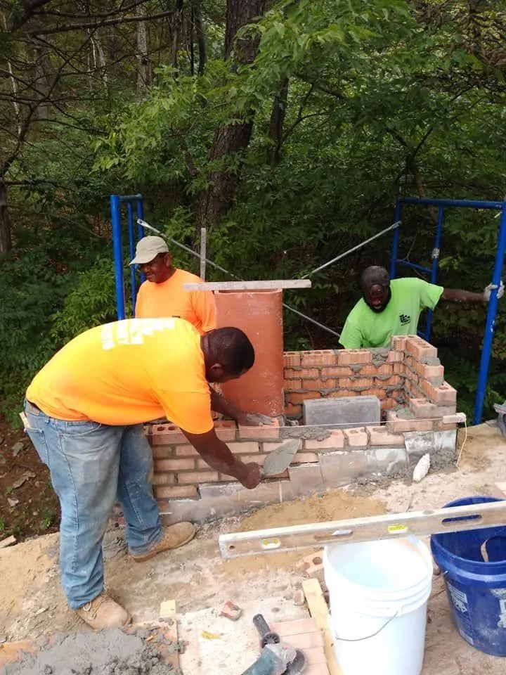 Workers building a brick structure outdoors, with tools and buckets beside them.