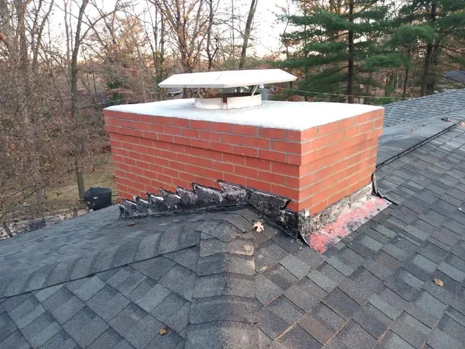Damaged chimney on a shingled roof with a white cap and black tar repair around its base