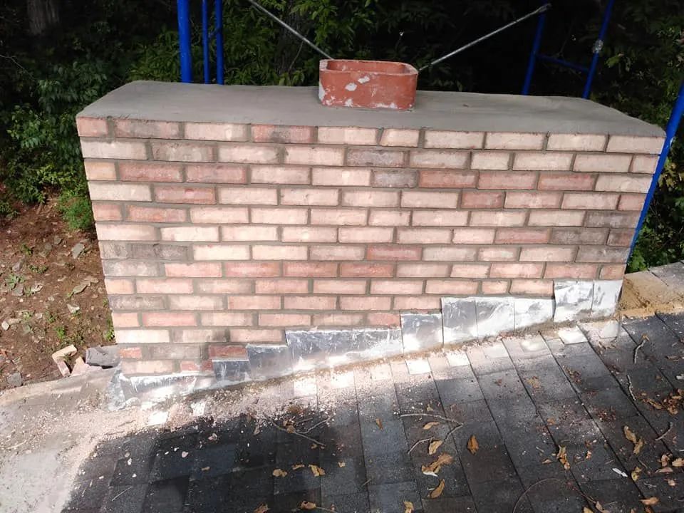 Brick wall with a loose brick on top and a damaged base along a wooden walkway outdoors