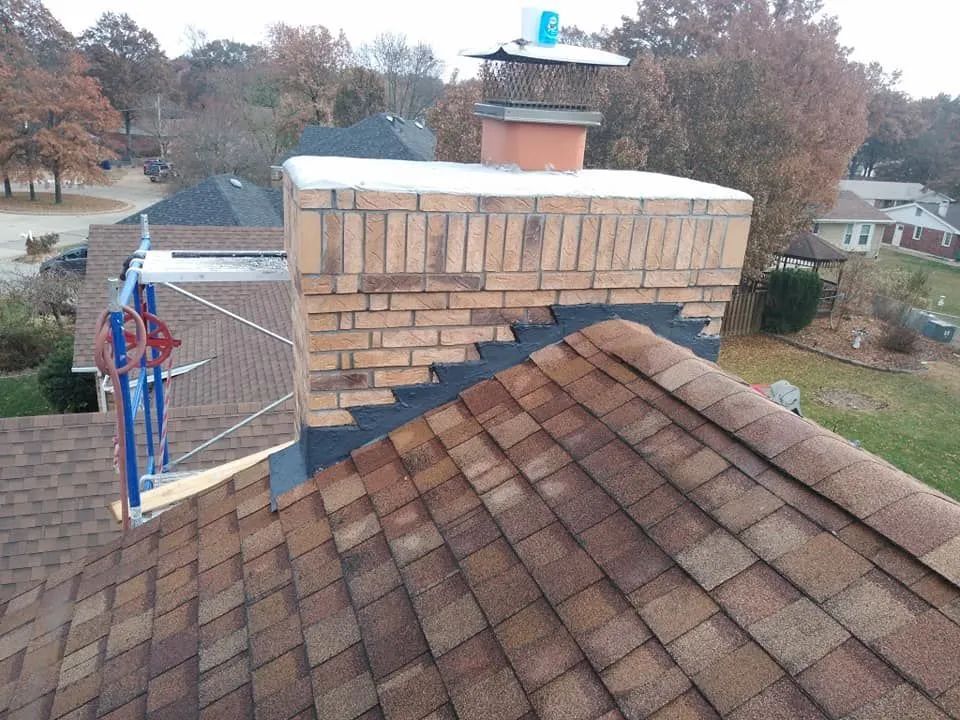 Brick chimney on a brown shingled roof beside a basketball hoop and suburban houses.