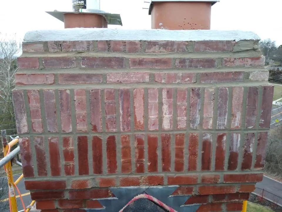 Brick chimney with red and tan masonry on a rooftop, with two vent pipes behind it.